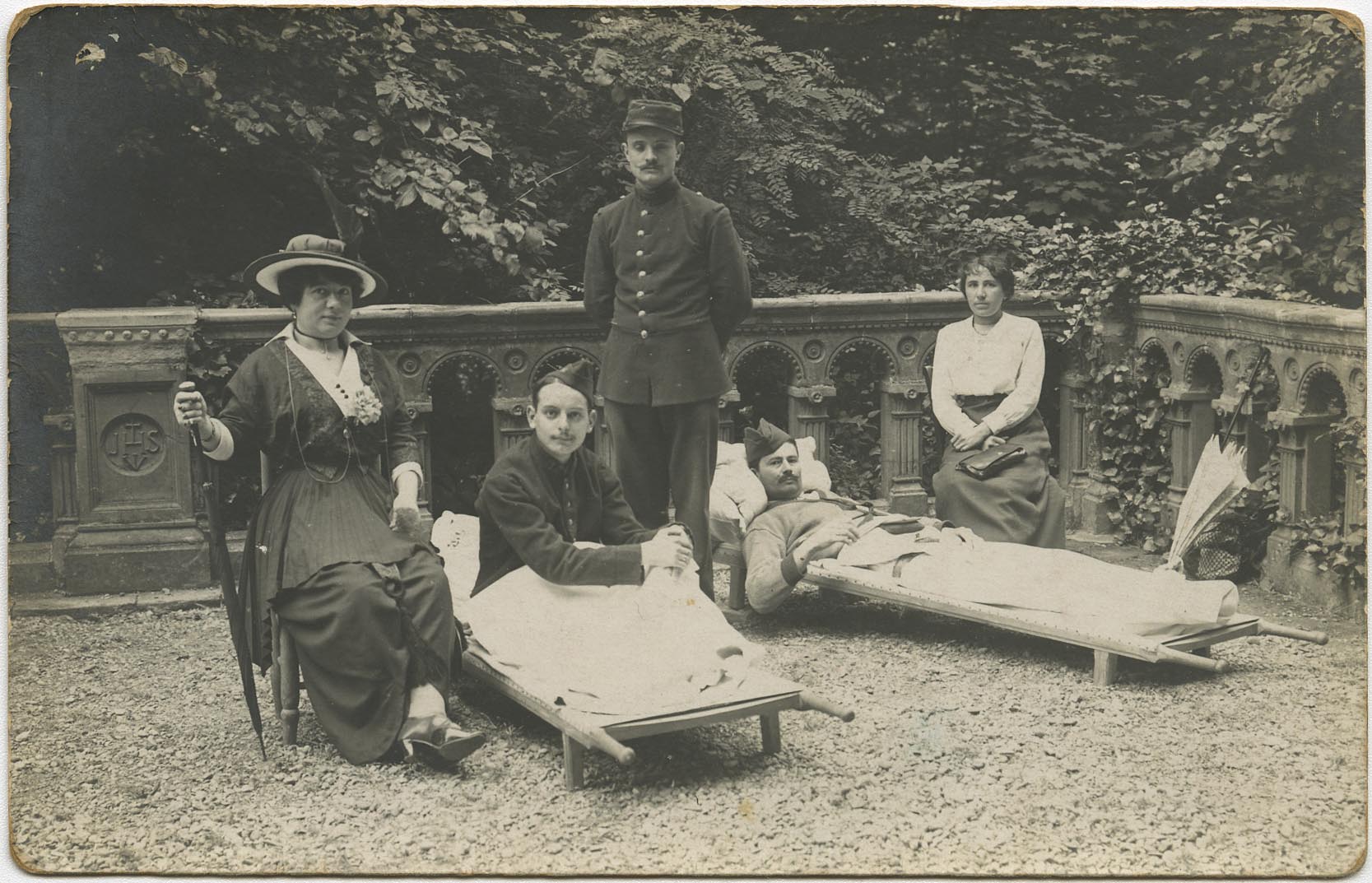 « Jules Sentenac pose entre deux soldats sur des brancards sur la terrasse du Caousou. Deux femmes se tiennent au chevet des blessés